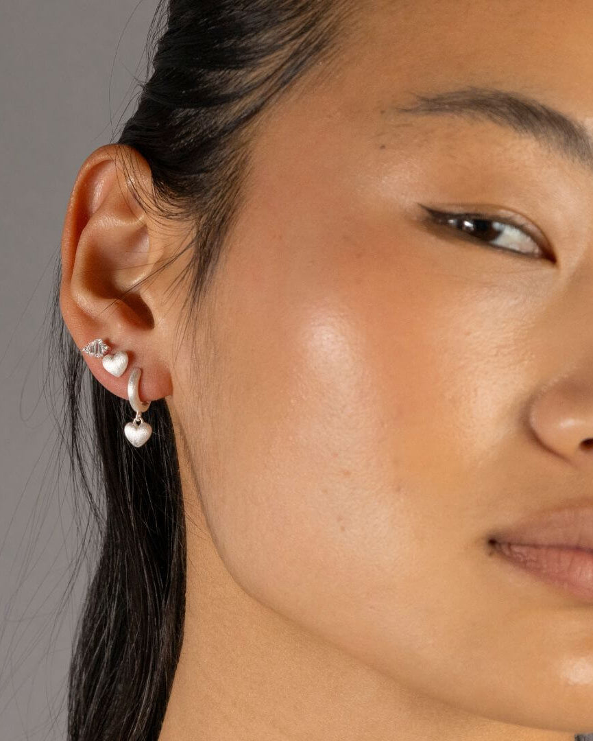 Jade wears silver heart huggie hoop earrings and matching heart stud earring