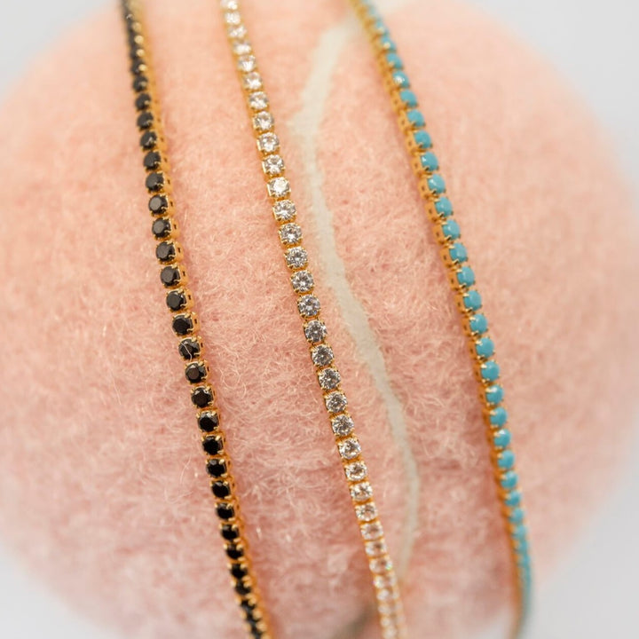 Selection of 18k gold vermeil tennis bracelet in black cubic zirconia, sparkly clear cubic zirconia and turquoise cubic zirconia on a tennis ball 