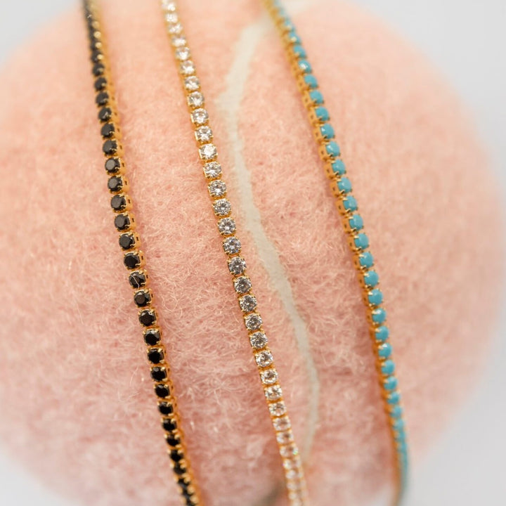 Selection of 18k gold vermeil tennis bracelet in black cubic zirconia, sparkly clear cubic zirconia and turquoise cubic zirconia on a tennis ball 