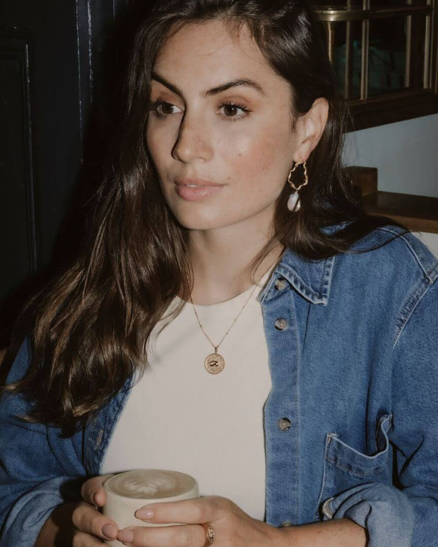 Close-up of a woman wearing gold hoop earrings and a ring, with a wider shot of her holding a cup.