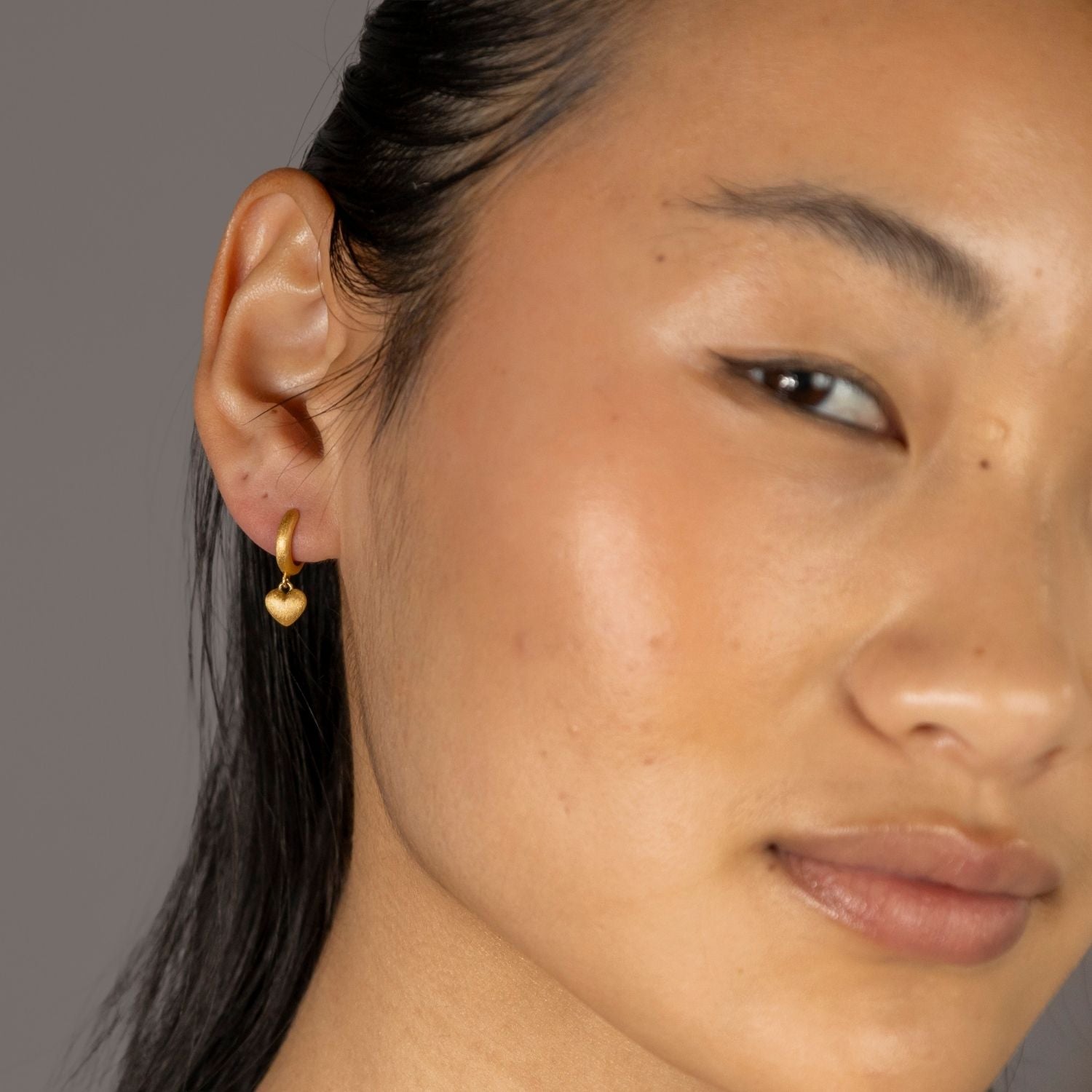 Close up of Jade wearing Brushed Heart Gold Huggie Hoops