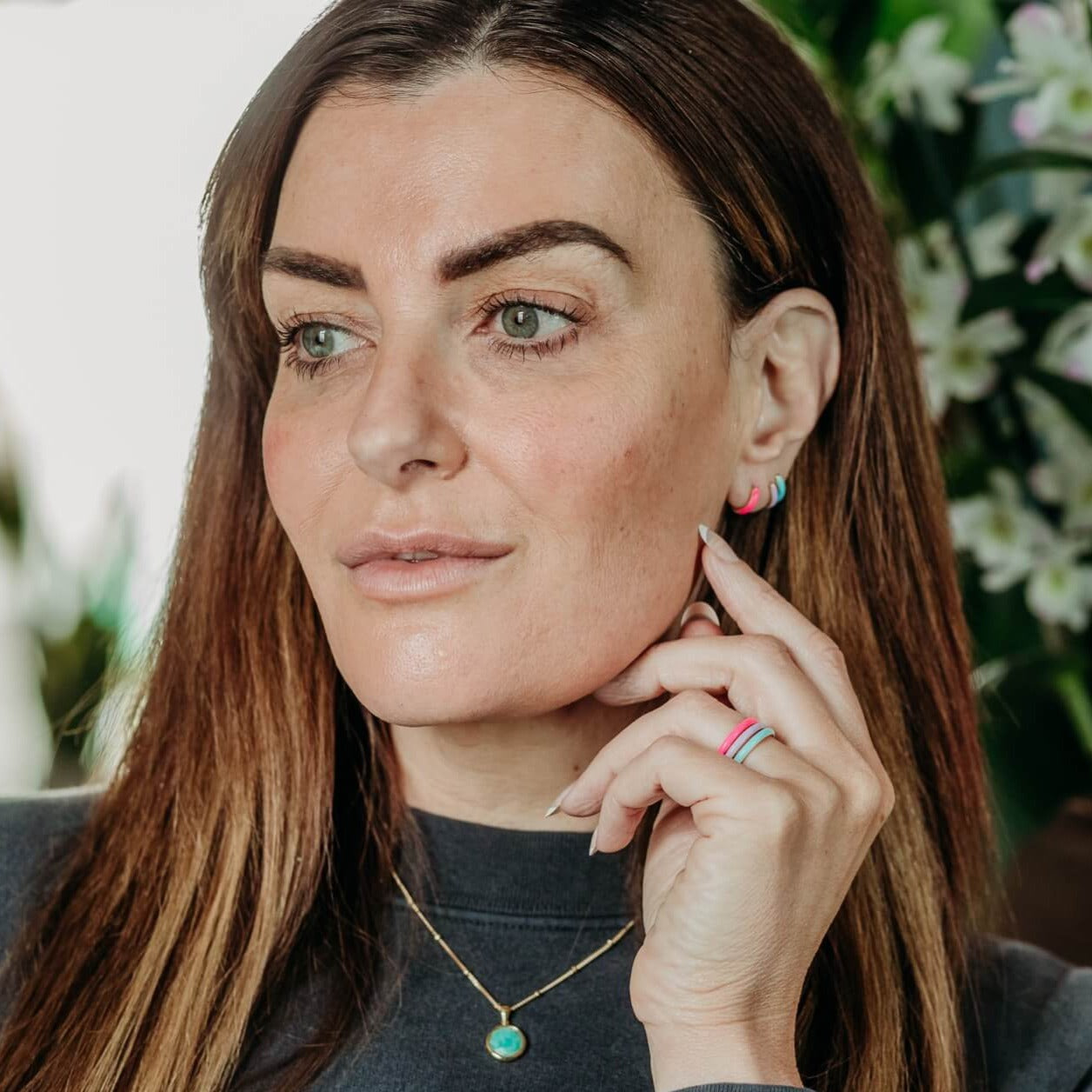 model wears coloured enamel huggie hoop earrings and coloured enamel stacking rings