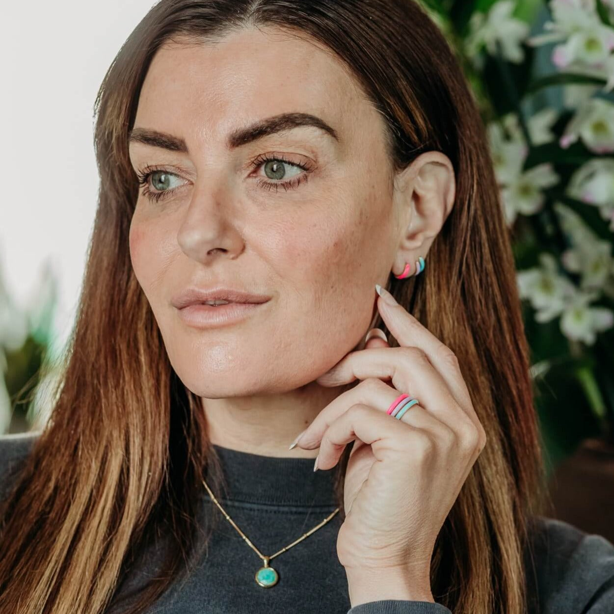 model wears enamel stacking rings and enamel huggie hoop earrings in pink, lavender and turquoise