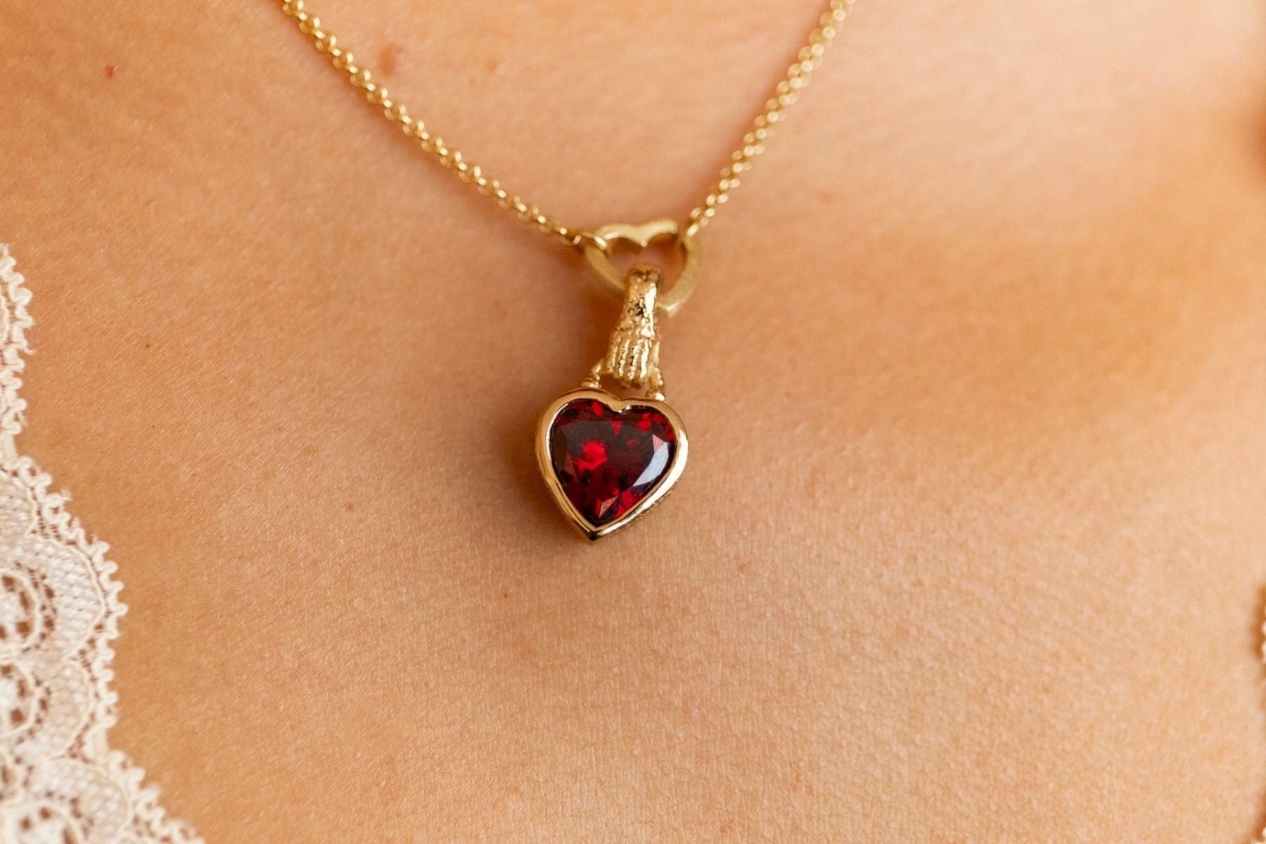model wears garnet hand in heart gold charm necklace on heart connector