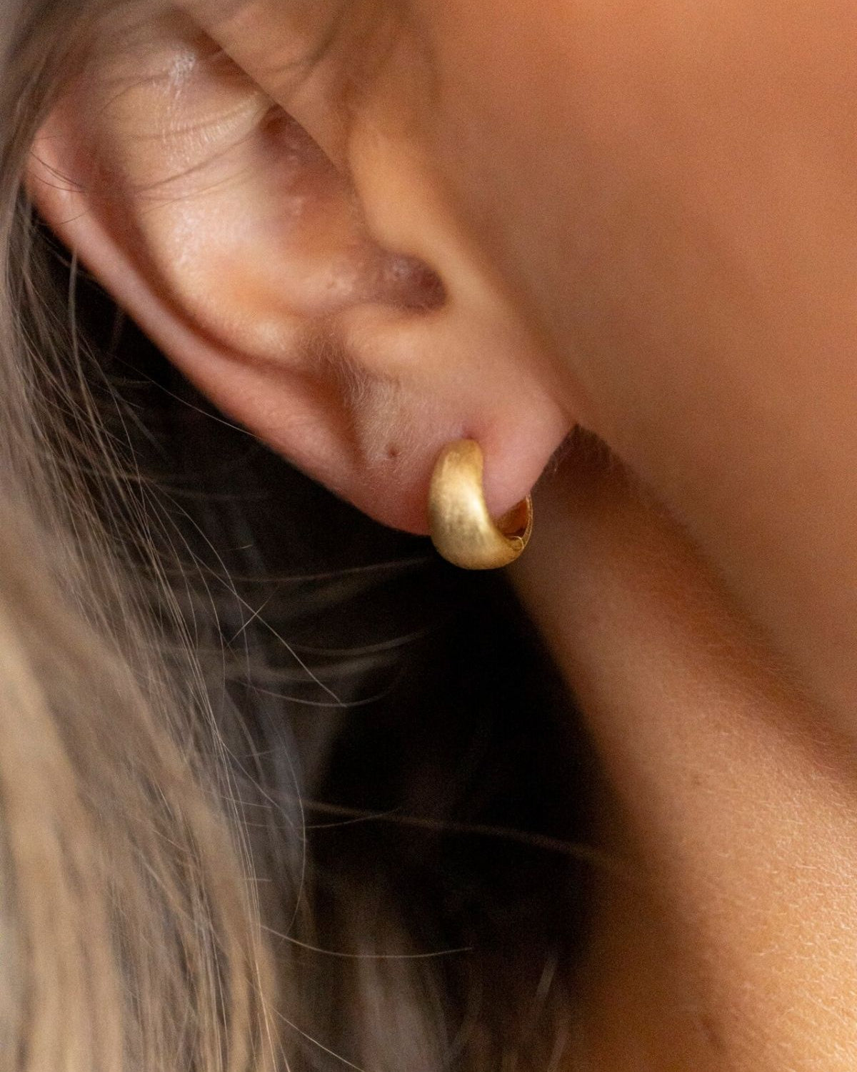 model wears Brushed Gold Chunky Huggie Hoops 
