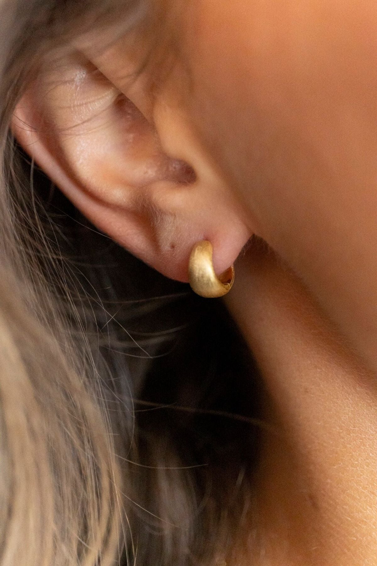 model wears Brushed Gold Chunky Huggie Hoops 
