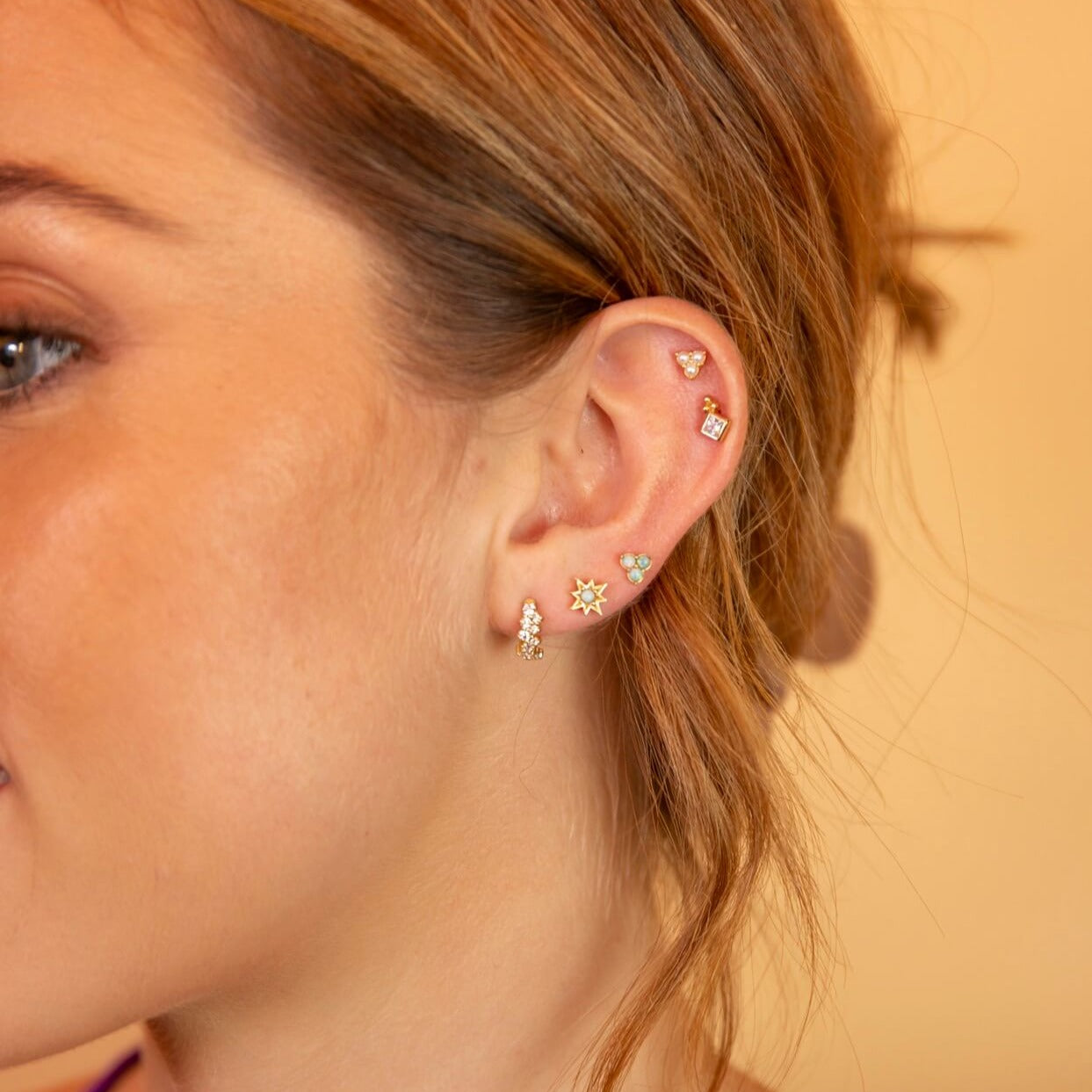 model wears gold earring ear stack including Opal Gold Star Mini Stud Earrings