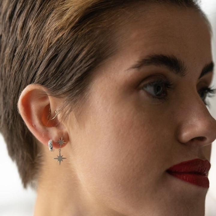 model wears silver brushed double north star stud earrings and silver sparkly star huggie hoop earrings
