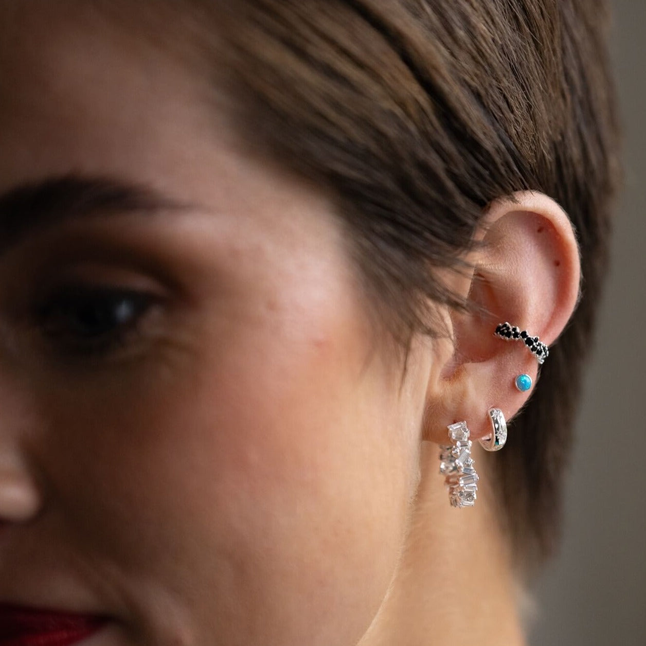 model wears silver ear stack of hoops and huggie earrings and Blue Opal and Silver Stud Earrings