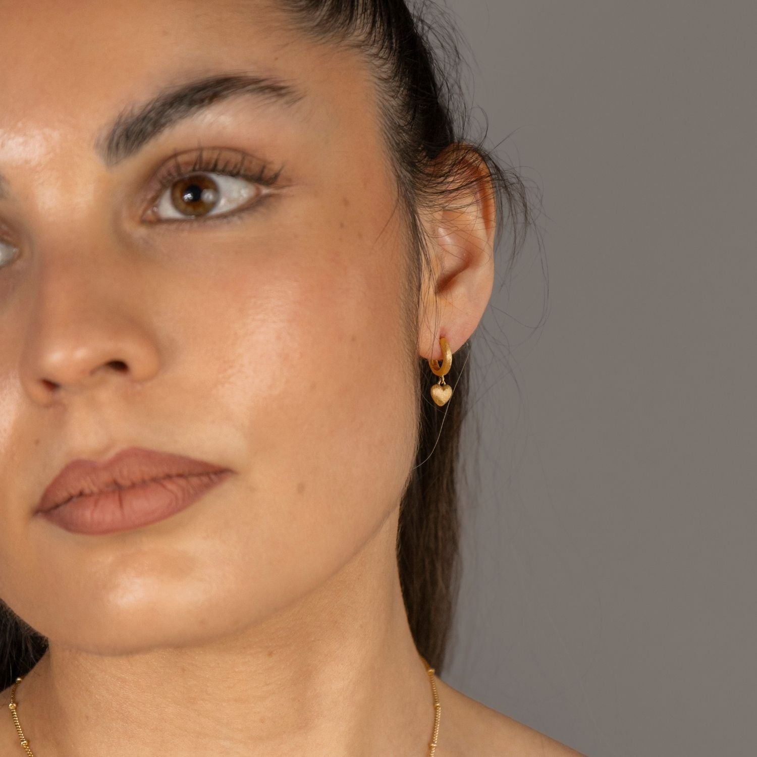 Nadia wears Brushed Heart Gold Huggie Hoops