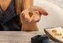 A close-up lifestyle shot of a person holding a gold heart-shaped pendant necklace in their hand and jewelry box visible on a wooden table in the foreground.