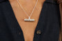 A close up of a woman wearing a silver T  bar pendant necklace with ruby and a silver ring with Know Your Worth 