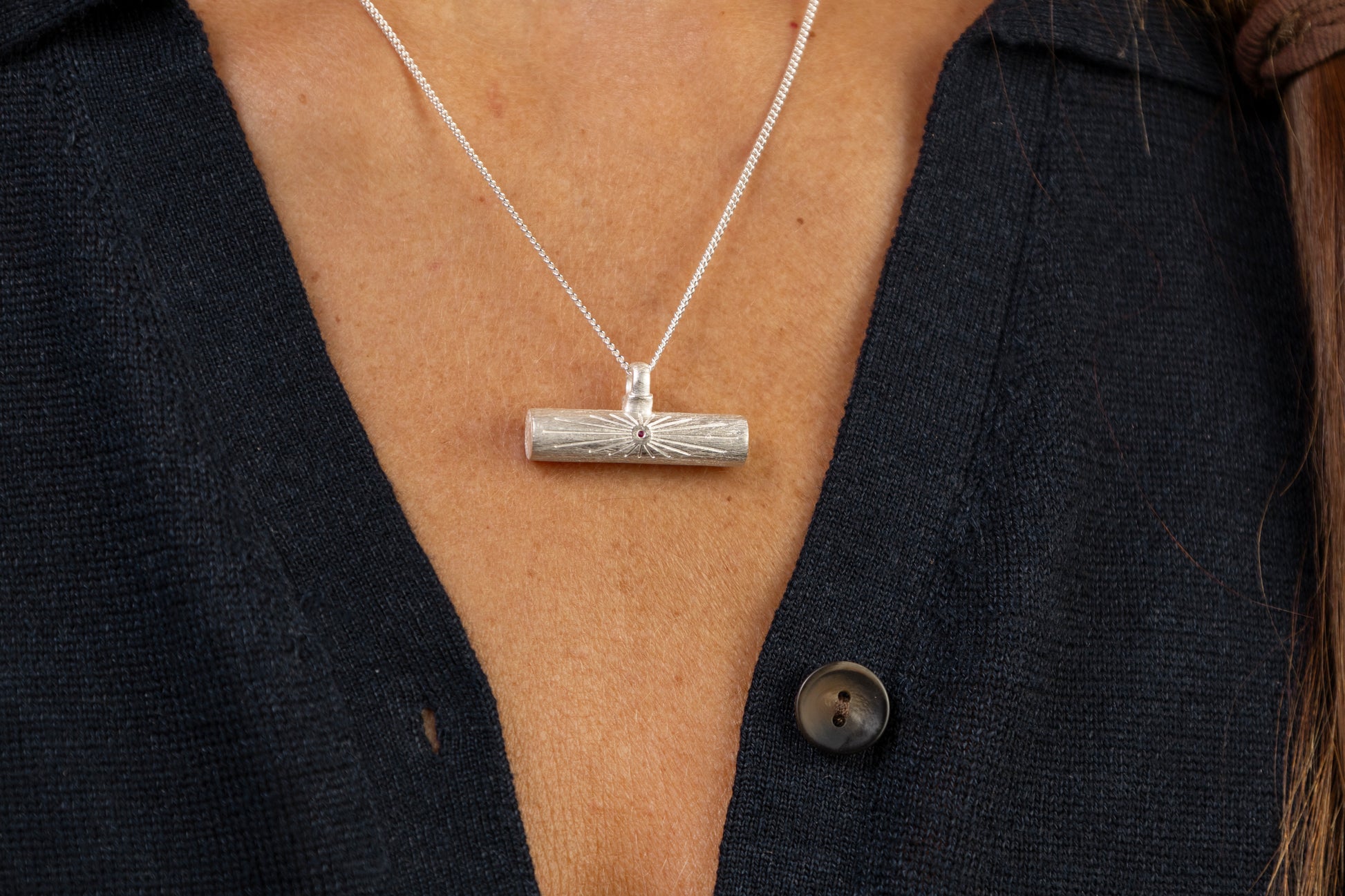 A close up of a woman wearing a silver T  bar pendant necklace with ruby and a silver ring with Know Your Worth 