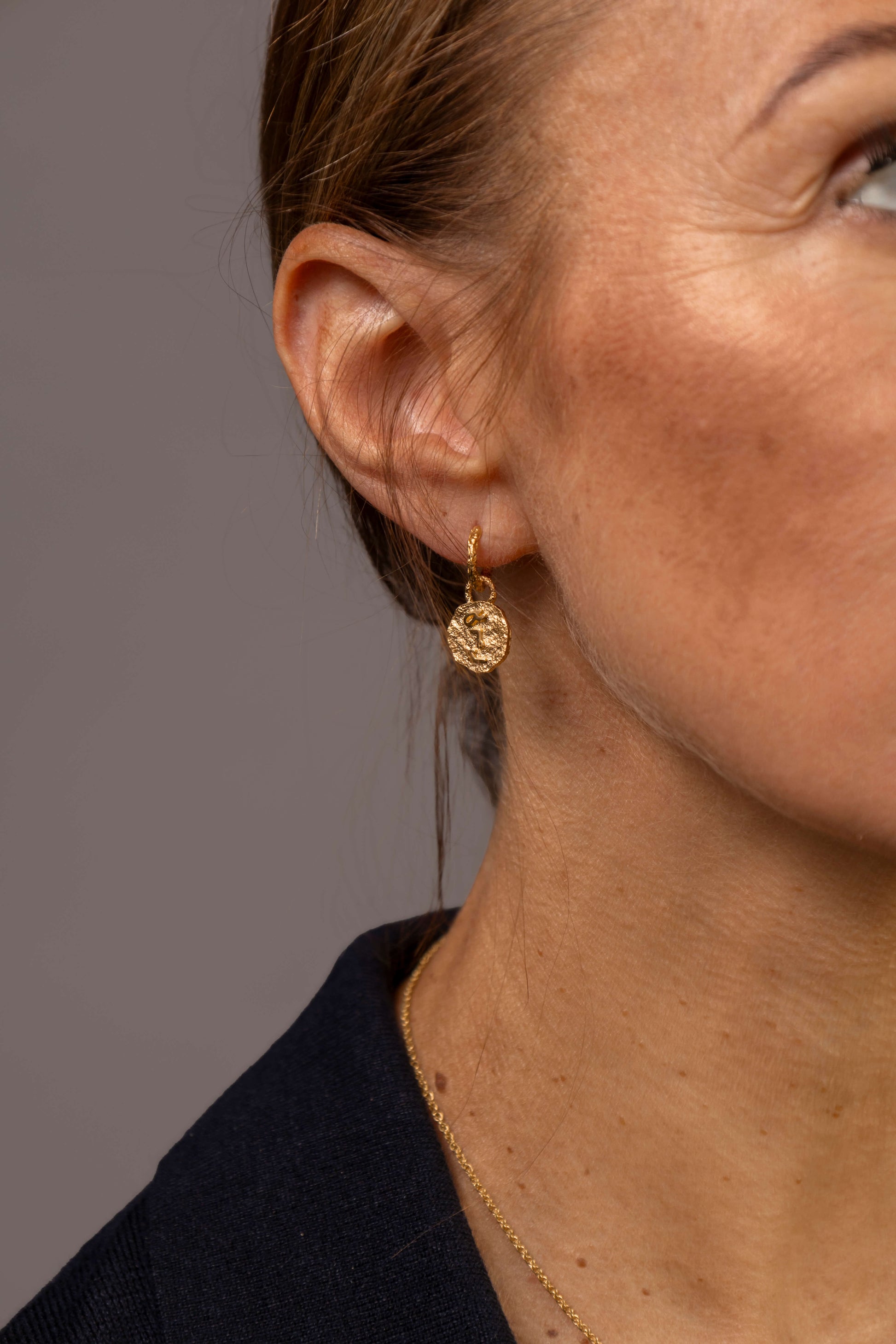 close up of a woman wearing gold vermeil coin huggie hoop earrings with F*** this S*** in the centre engraved in Teeline Shorthand