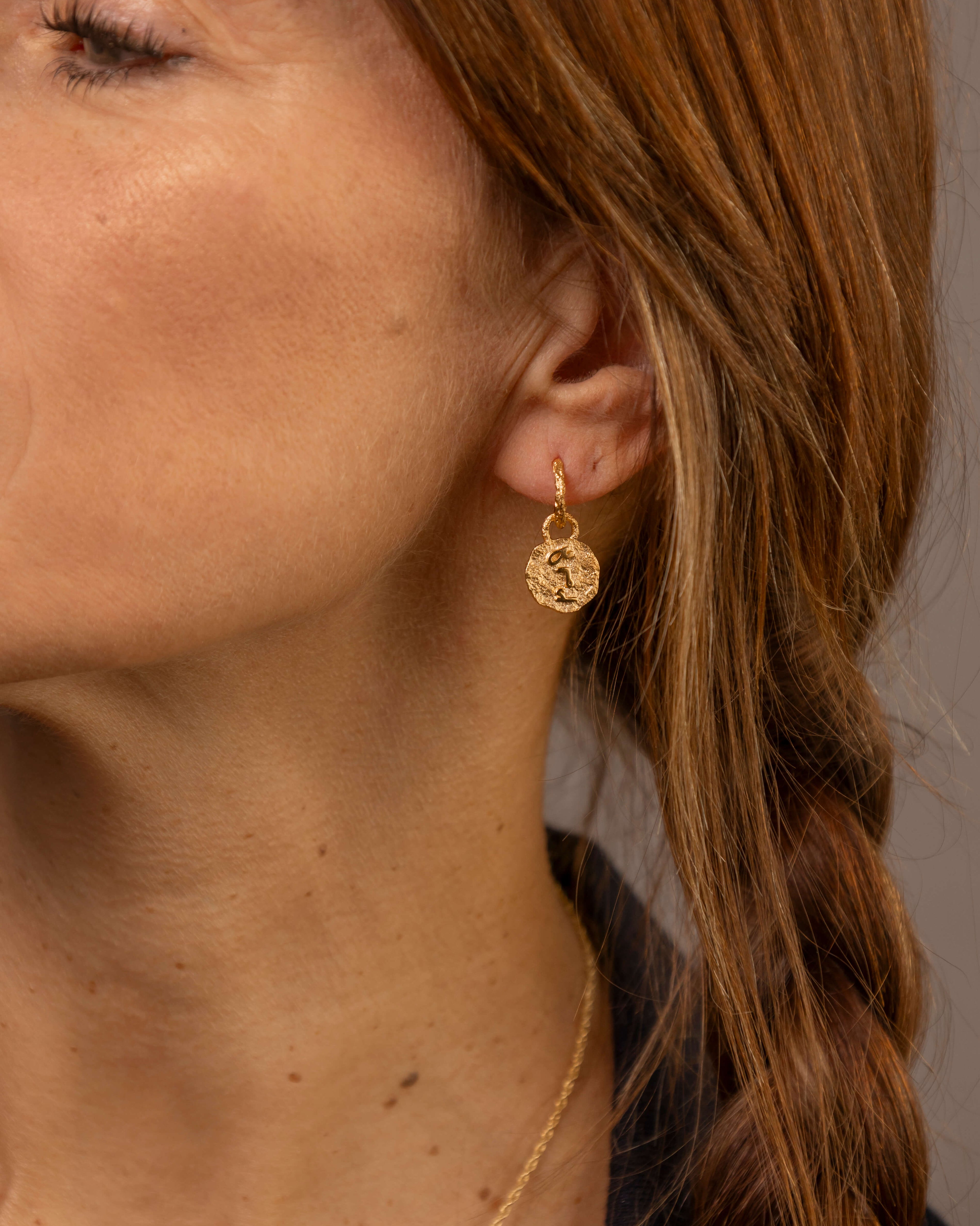 close up of a woman wearing gold vermeil coin huggie hoop earrings with F*** this S*** in the centre engraved in Teeline Shorthand