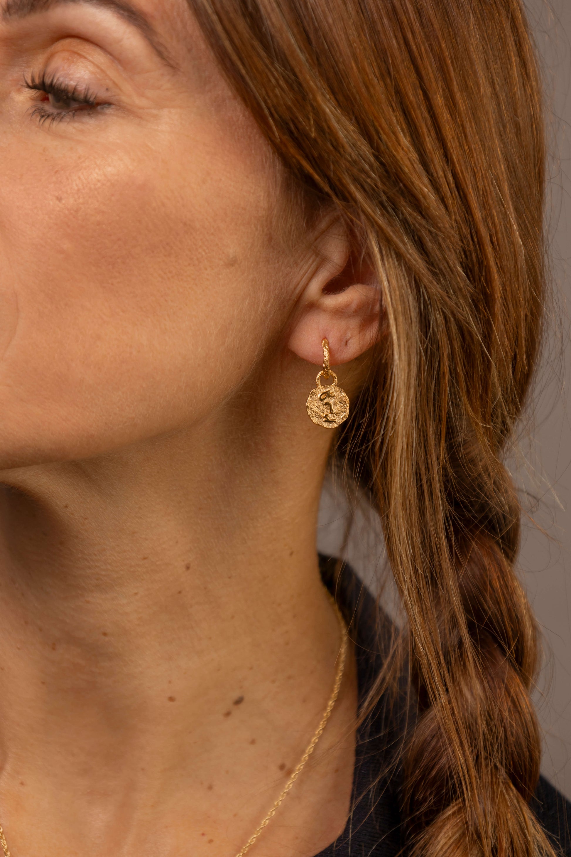 close up of a woman wearing gold vermeil coin huggie hoop earrings with F*** this S*** in the centre engraved in Teeline Shorthand