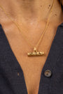 A close-up of a person wearing a textured gold T bar pendant necklace with a F*** this S*** inscribed in Teeline Shorthand, paired with a dark navy button-up shirt.