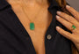 A close-up lifestyle shot of a woman wearing a gold chain necklace with a green chacledony gemstone rectangular pendant engraved with F*** this S*** in Shorthand, and wearing a matching green ring on her finger.