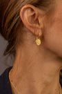 Close up of woman's ear wearing gold textured hoop earrings with coin pendants which say Know Your Worth in Shorthand 