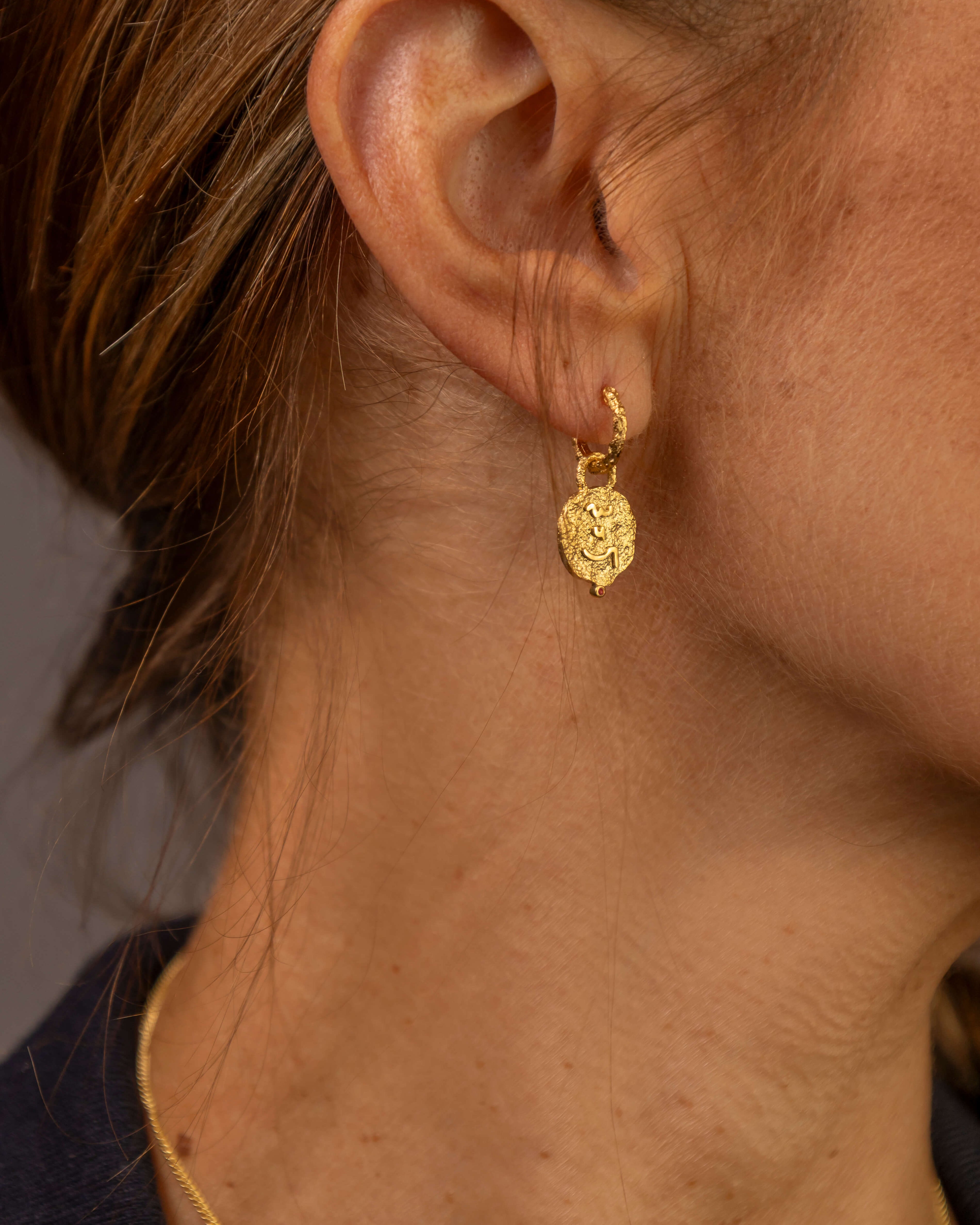 Close up of woman's ear wearing gold textured hoop earrings with coin pendants which say Know Your Worth in Shorthand 