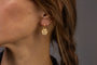 Close up of woman's ear wearing gold textured hoop earrings with coin pendants which say Know Your Worth in Shorthand 