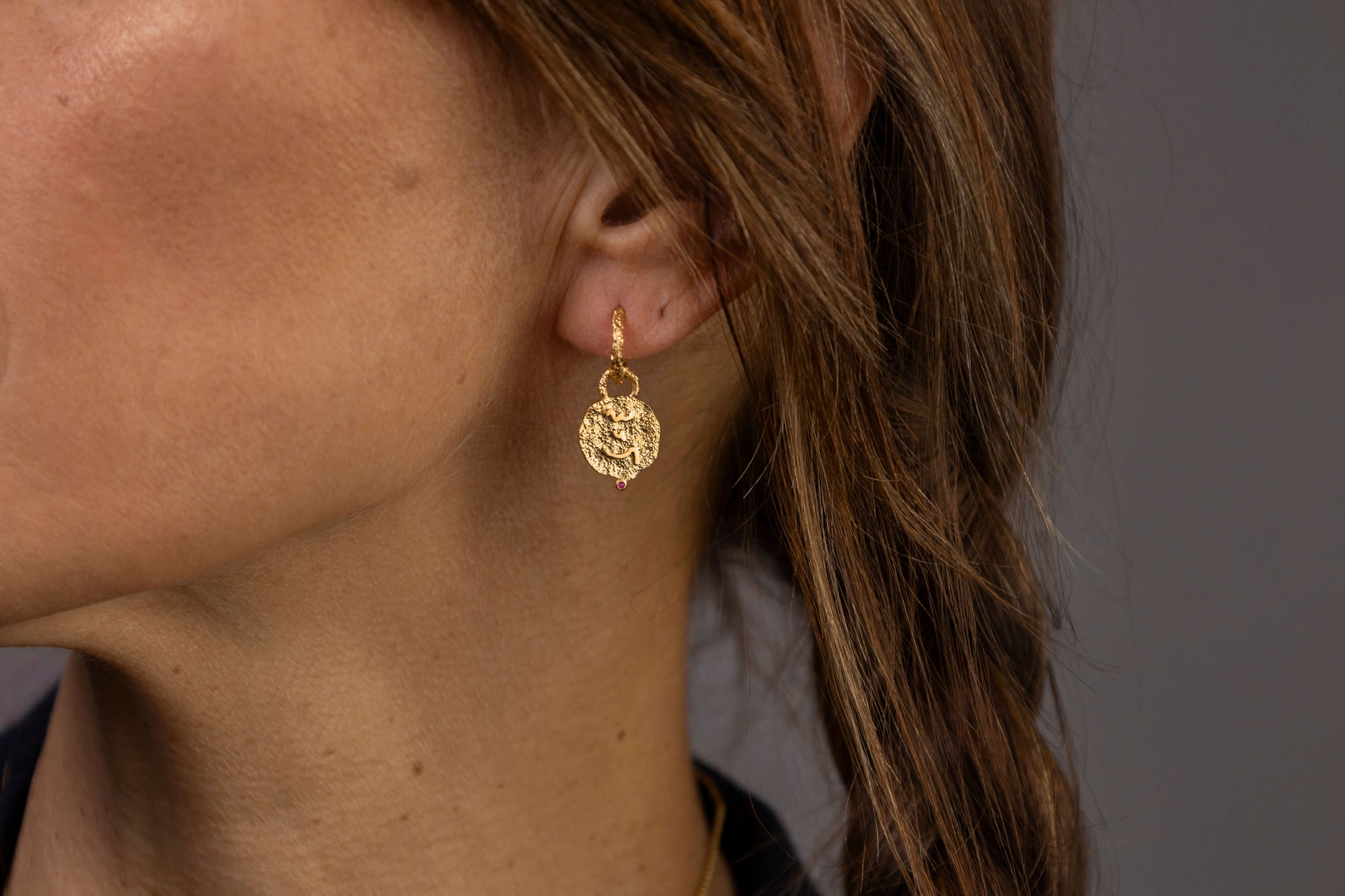 Close up of woman's ear wearing gold textured hoop earrings with coin pendants which say Know Your Worth in Shorthand 