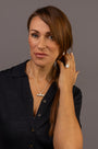 A woman with brown hair is shown from the chest up against a solid gray studio background, wearing a silver T  bar pendant necklace and a silver ring with Know Your Worth inscribed on both  in Teeline Shorthand 
