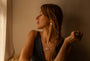 A woman with long brown hair in a side braid is shown in profile, wearing a silver T bar pendant necklace and a silver ring inscribed with Difficult Woman in Teeline Shorthand, set against a warm, dimly lit beige wall.